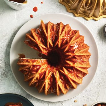 Golden bundt cake with caramel glaze on white plate, Nordic Ware Cut Crystal bundt pan visible in background