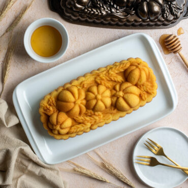 Wheat & Pumpkin Loaf on plate surrounded by pan, dish of honey, honeycomb stick dipped in honey
