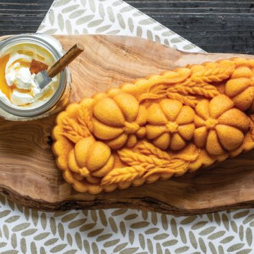 Golden cornbread loaf baked in Nordic Ware wheat-shaped aluminum pan, served on plate with honey cream cheese