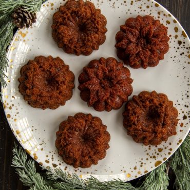 Six golden mini wreath cakes from Nordic Ware Wreathlettes pan arranged on white plate with holiday decorations