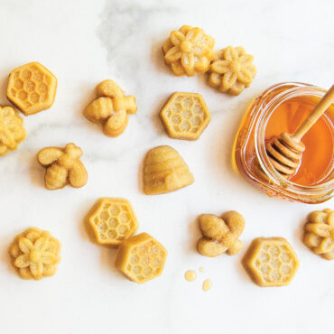 Golden bee-shaped bitelets baked in Nordic Ware aluminum pan, arranged on marble surface with honey jar