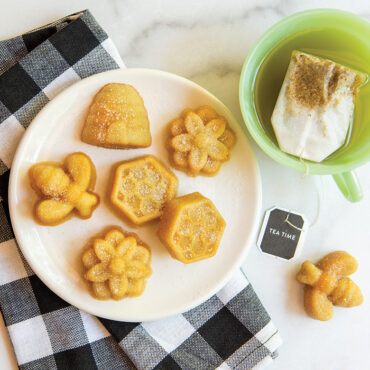 Small golden bee-shaped cakes arranged on white plate, baked using Nordic Ware Busy Bee Bitelet pan