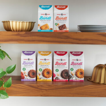 Nordic Ware bundt cake mix collection displayed on wooden shelves with bronze bundt pans