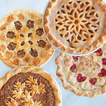Four baked pies with decorative lattice tops showing heart, leaf, and geometric patterns made with Nordic Ware pie cutters