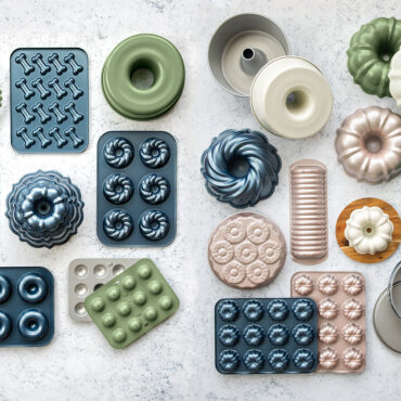 Collection of Nordic Ware aluminum baking pans in various shapes including bundt, tube, and loaf pans with natural silver finish