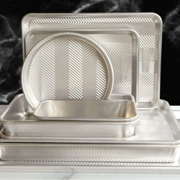 Nordic Ware Prism collection aluminum baking pans stacked, featuring textured chevron pattern in natural finish
