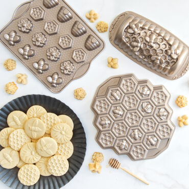 Nordic Ware aluminum bee-themed baking pans with golden honey cookies - Busy Bee Bitelet, Honey Hive Loaf, and Honeycomb Pull-Apart pans