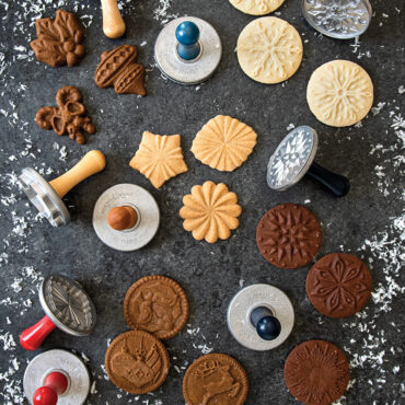 Nordic Ware wooden cookie stamps with star and snowflake designs alongside decorated sugar cookies