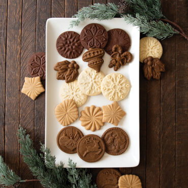 Golden baked gingerbread cookies with decorative stamped patterns arranged on white plate with kitchen towel