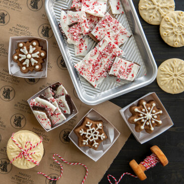 Decorated sugar cookies with snowflake patterns next to Nordic Ware cookie stamps in festive gift display