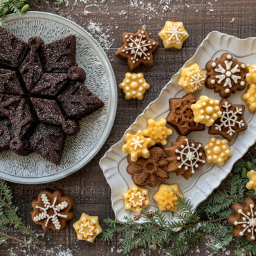 Six golden snowflake-shaped cakes displayed on white plates, showing intricate detailed patterns from Nordic Ware cakelet pan