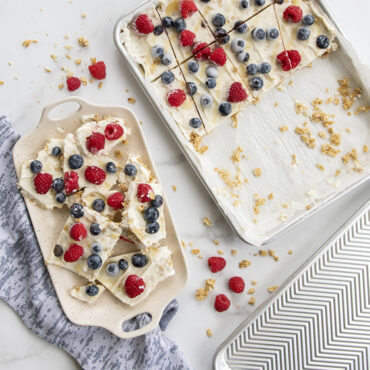 Colorful yogurt bark with berries in Nordic Ware aluminum quarter sheet pan, with cut pieces on tray beside it