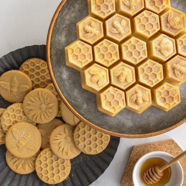 Golden baked sugar cookies with honeybee stamps and honeycomb bundt cake displayed on white serving plates