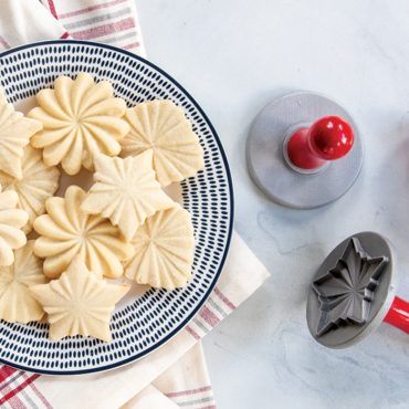 Golden baked cookies with decorative pleated patterns on white plate, Nordic Ware cookie stamps beside