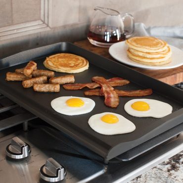 Nordic Ware aluminum double backsplash griddle on stovetop with cooked eggs, bacon, sausage and pancakes