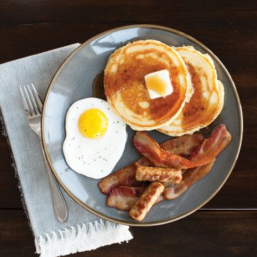 Breakfast plate with golden pancakes, sunny-side up eggs, crispy bacon and sausage cooked on Nordic Ware griddle