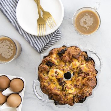 Baked egg casserole in Nordic Ware aluminum bundt pan with golden-brown top, served with coffee cups and fresh eggs