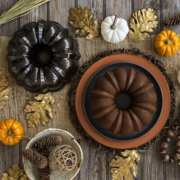 Nordic Ware bronze bundt pan next to golden spice bundt cake on autumn table setting with fall decorations