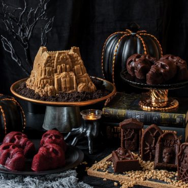 Halloween scene with Nordic Ware skull cakelet pan, decorated skull-shaped cakes, bundt cake, and spooky tombstone treats