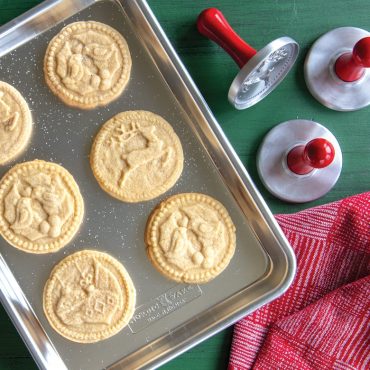 Golden sugar cookies with holiday designs on Nordic Ware aluminum quarter sheet pan with cookie stamps