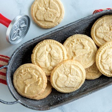 Golden baked cookies with Christmas designs stamped in black cast iron tray with Nordic Ware cookie stamps
