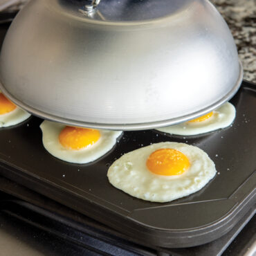 Nordic Ware aluminum high dome grill lid covering fried eggs on dark griddle, silver finish dome shape