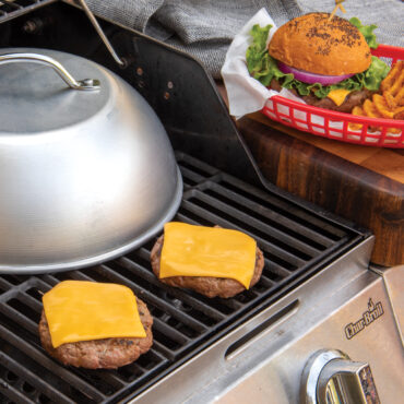 Aluminum high-dome grill lid covering cheeseburgers with melted yellow cheese on grill grates