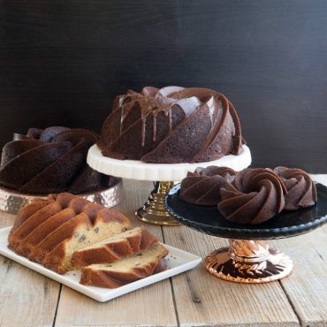 Four Heritage bundt cakes in different sizes: chocolate bundt on pedestal, mini bundts on plate, sliced vanilla loaf with nuts
