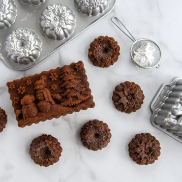 Golden baked wreath-shaped cakes from Nordic Ware Wreathlettes pan with detailed festive design on marble surface