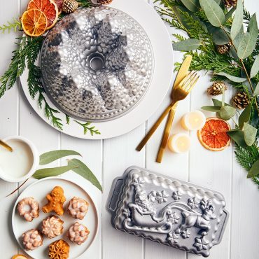 Nordic Ware Pine Forest bundt pan with baked cake, Santa sleigh loaf pan, and mini tea cakes displayed