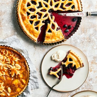 Baked lattice-topped pie with golden crust cut into triangular slice on white plate beside whole pie