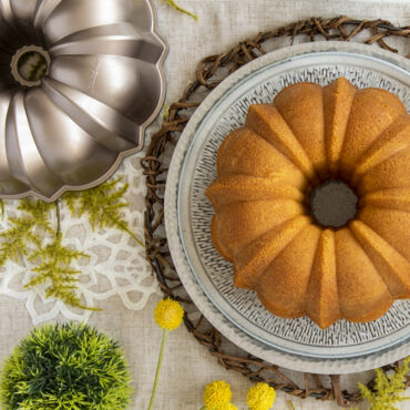 Golden bundt cake on white platter beside Nordic Ware Toffee aluminum bundt pan with decorative fluted design