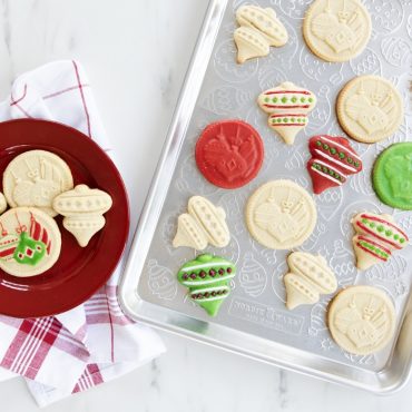 Nordic Ware aluminum baking sheet with ornament embossed surface holding stamped and decorated holiday cookies