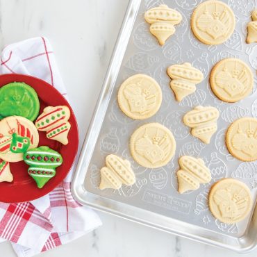 Baked golden cookies with embossed ornament patterns on Nordic Ware aluminum half sheet pan