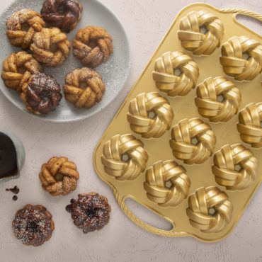 Cast aluminum mini bundt pan with braided design pattern, displaying six golden baked mini bundt cakes
