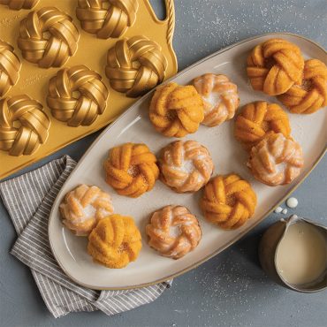 Nordic Ware aluminum mini bundt pan with six braided-pattern cavities, displaying glazed golden cakes