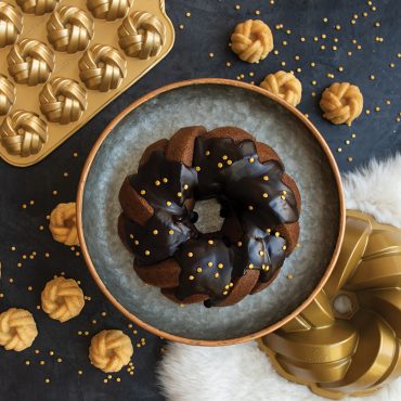 Two chocolate bundt cakes with decorative braided pattern next to gold-colored Nordic Ware aluminum bundt pans