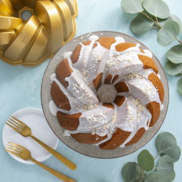Golden glazed bundt cake with braided rope design next to Nordic Ware aluminum bundt pan and serving plate