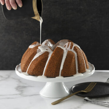 White glaze being poured over golden bundt cake in Nordic Ware 75th Anniversary Braided Bundt pan