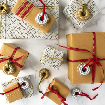 Two silver cast aluminum ornaments shaped like miniature bundt pans with wrapped gift boxes beneath them