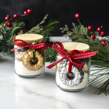 Two cast aluminum bundt ornaments, one silver and one gold, tied to glass jar filled with baking ingredients