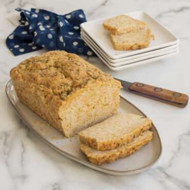 Sliced golden beer cheese bread on white platter, baked in Nordic Ware Naturals loaf pan