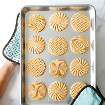 Two Nordic Ware Bundt-shaped silicone hot pads holding aluminum half sheet pan with golden baked cookies