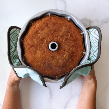 Nordic Ware silicone hot pads holding aluminum bundt pan with golden baked cake, fluted design visible