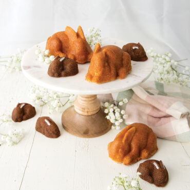 Six golden-brown bunny-shaped cakelets arranged together, showing detailed ears and face features from Nordic Ware baking pan