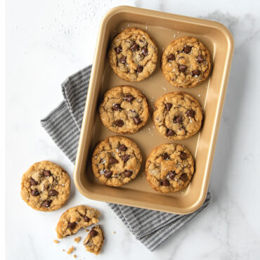 Small rectangular aluminum baking sheet with nonstick surface displaying golden-brown mini cookies, one cookie beside pan
