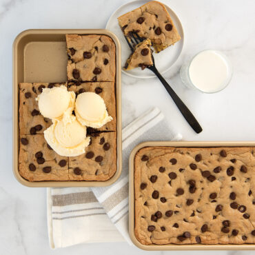 Small rectangular Nordic Ware nonstick baking sheet with golden sheet pan cookie, one slice cut and topped with vanilla ice cream