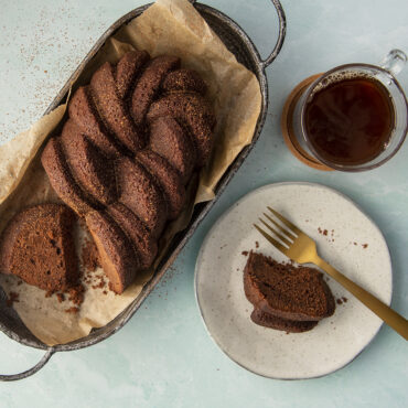 Golden braided loaf cake with textured surface on white plate, baked in Nordic Ware aluminum braided loaf pan