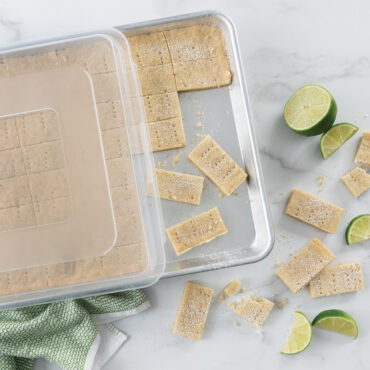 Nordic Ware aluminum half sheet pan with clear lid, containing golden baked bars cut into squares