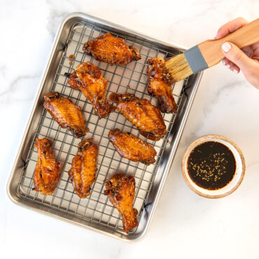 Raw chicken wings being basted with marinade on Nordic Ware aluminum quarter sheet pan with cooling grid